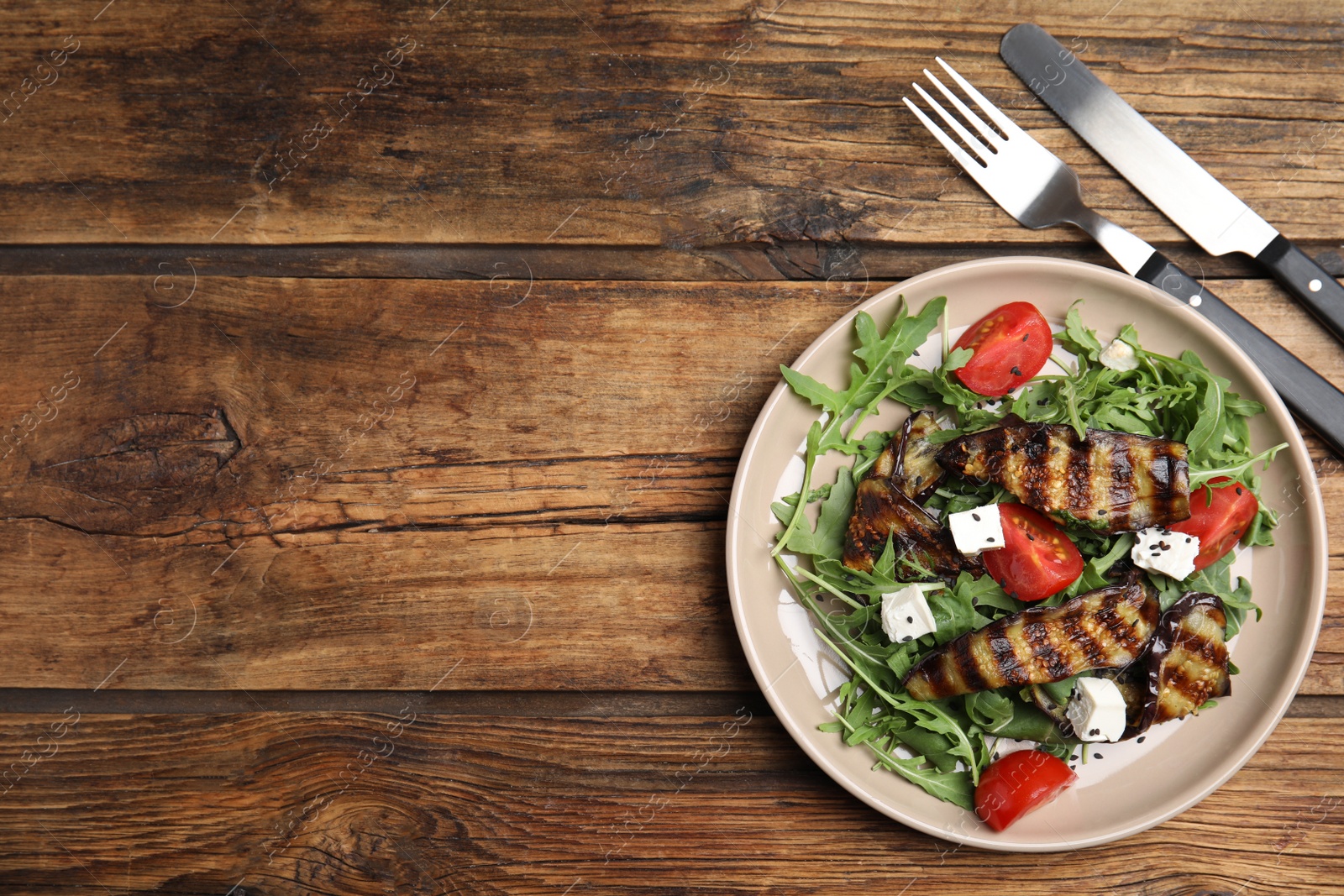 Photo of Delicious salad with roasted eggplant, feta cheese and arugula served on wooden table, flat lay. Space for text