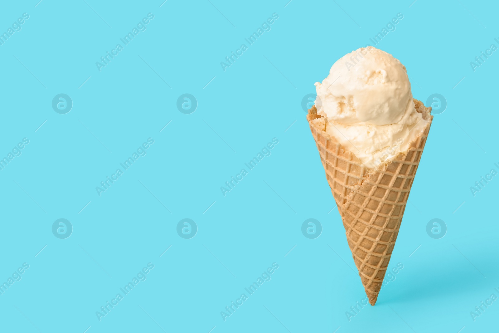 Photo of Delicious ice cream in waffle cone on light blue background. Space for text