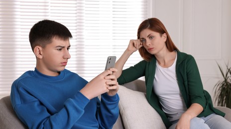 Photo of Boy using smartphone and ignoring his upset mother at home. Teenager problems