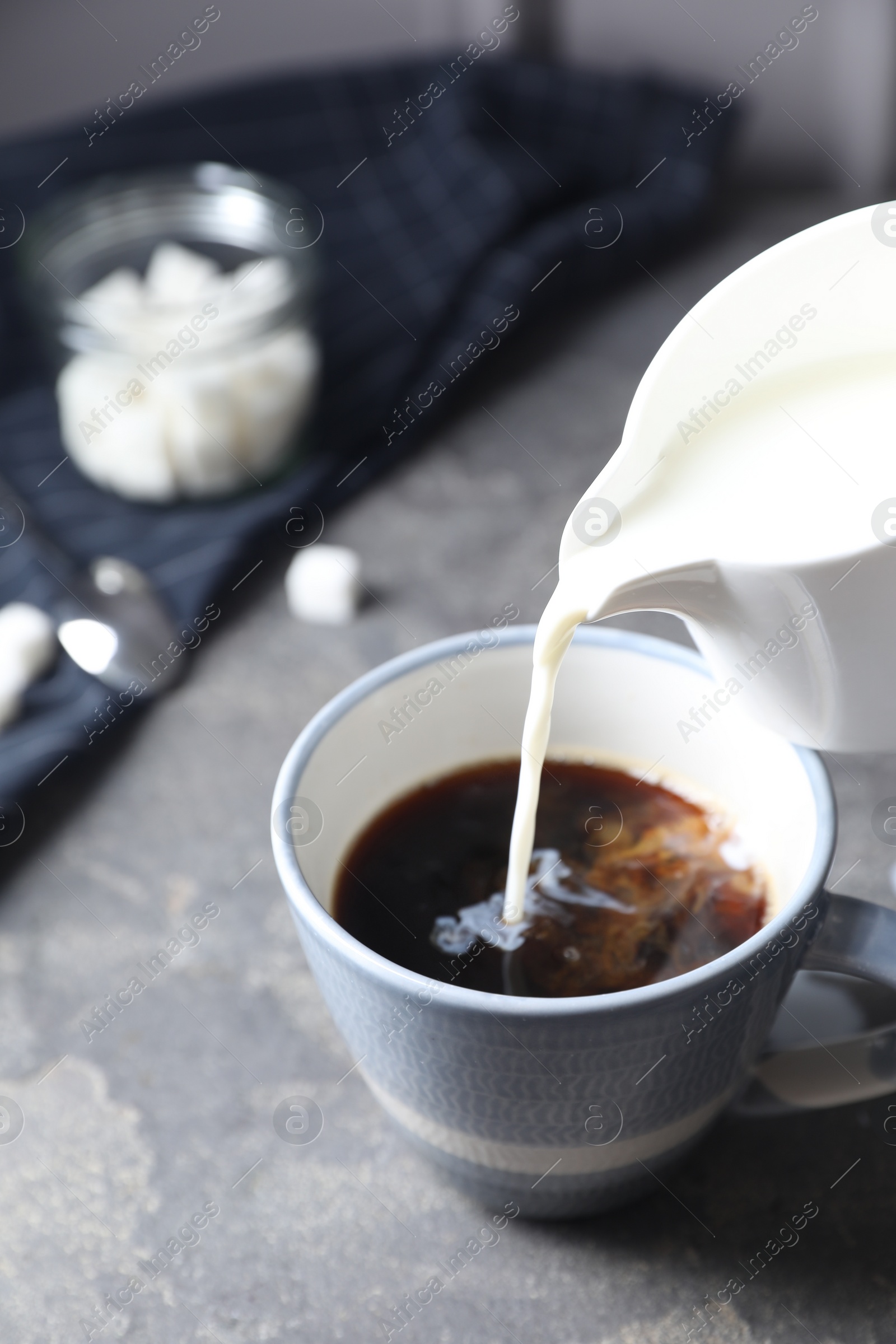 Photo of Pouring milk into cup of coffee on grey table, closeup