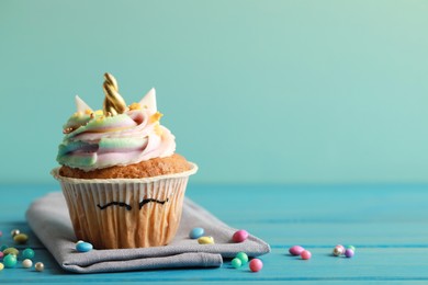 Photo of Cute sweet unicorn cupcake on light blue wooden table, space for text