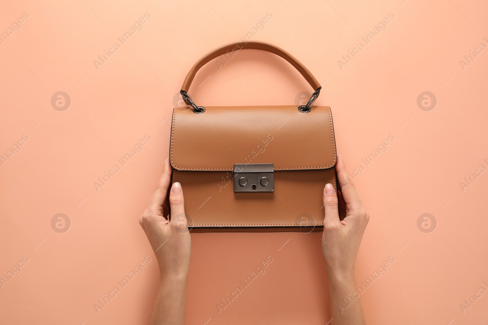 Photo of Woman holding stylish handbag on beige background, closeup