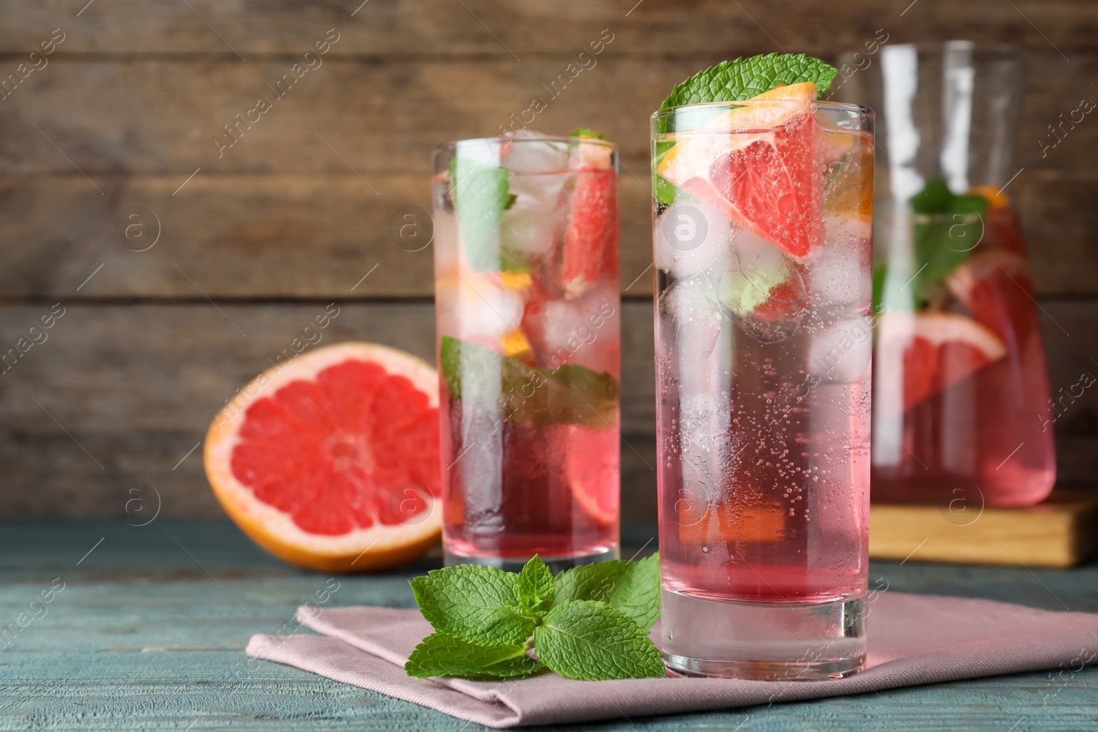 Photo of Delicious grapefruit lemonade with soda water and mint on blue wooden table. Fresh summer cocktail