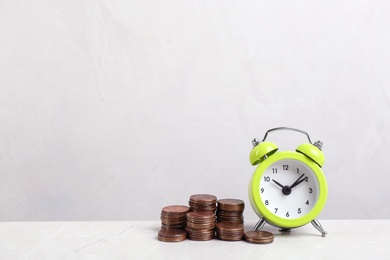 Photo of Light green alarm clock and stacked coins on light grey marble table, space for text. Money savings