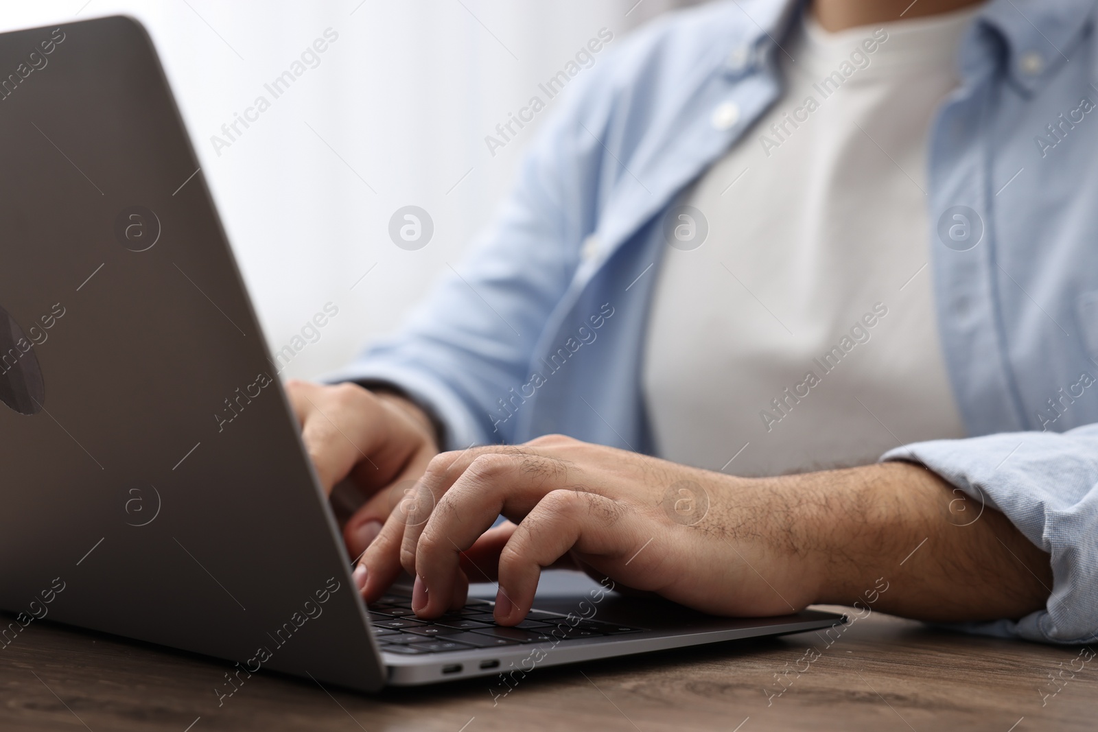 Photo of E-learning. Young man using laptop at wooden table, closeup