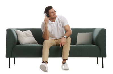 Man with laptop listening to music on comfortable green sofa against white background