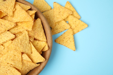 Wooden bowl of tasty Mexican nachos chips on light blue background, top view