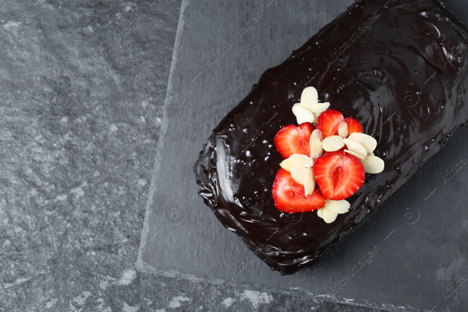 Photo of Delicious chocolate sponge cake with strawberry and almond flakes on black table, top view. Space for text