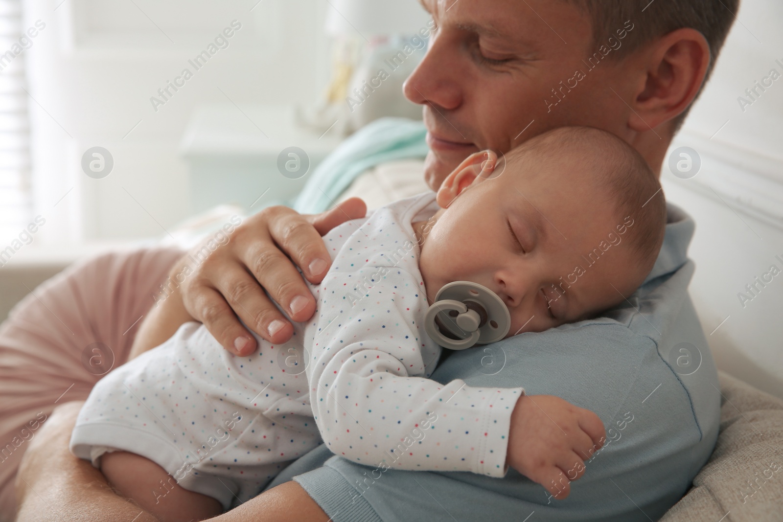 Photo of Happy father holding his cute sleeping baby with pacifier at home