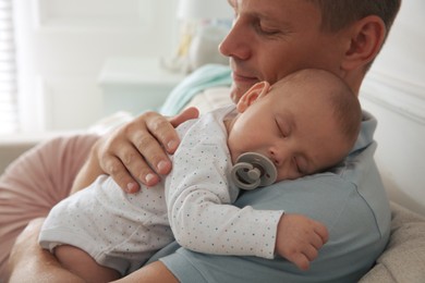 Happy father holding his cute sleeping baby with pacifier at home