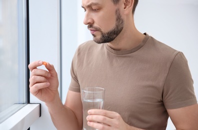 Young man taking pill indoors