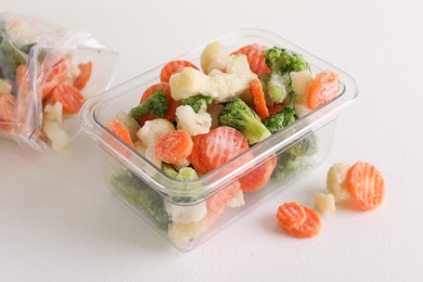 Photo of Mix of different frozen vegetables in plastic container on white textured table