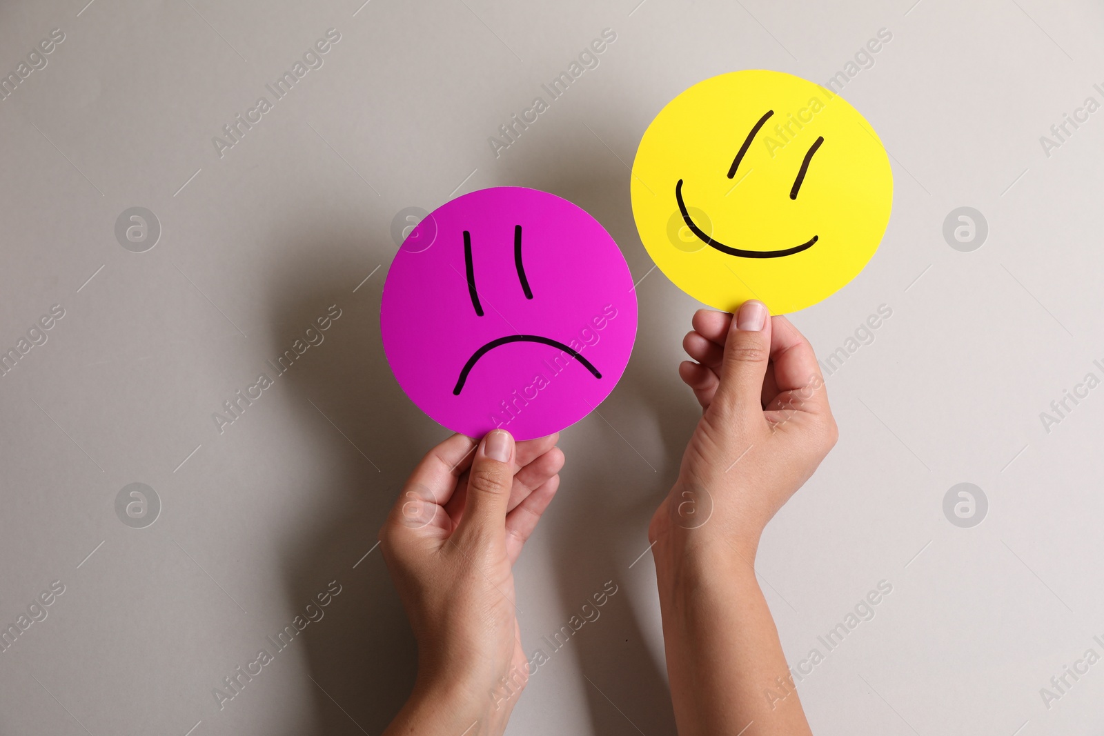 Photo of Choice concept. Woman holding papers with sad and happy emoticons on light grey background, closeup