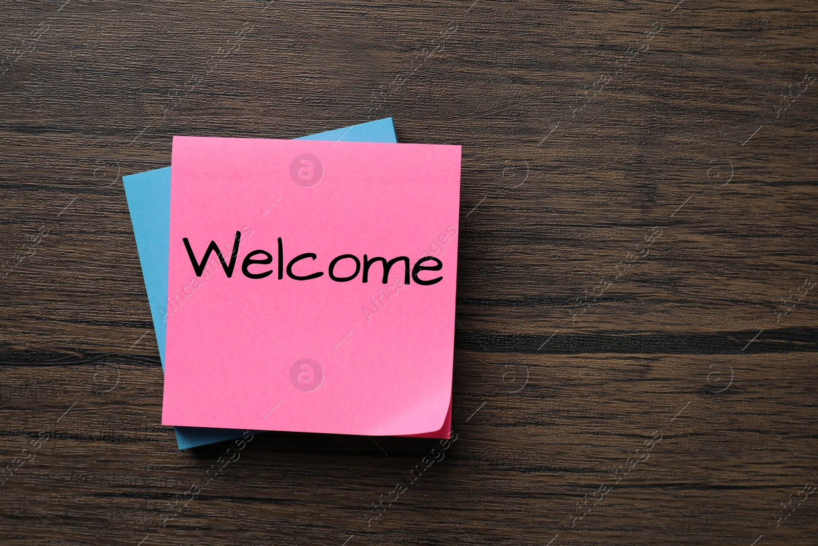 Image of Paper note with word Welcome on wooden table, top view. Space for text