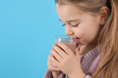 Photo of Cute little child drinking tasty chocolate milk on light blue background, closeup. Space for text