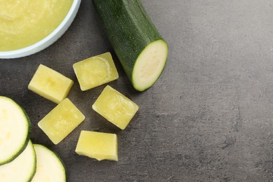 Photo of Frozen zucchini puree cubes and fresh zucchini on grey table, flat lay. Space for text