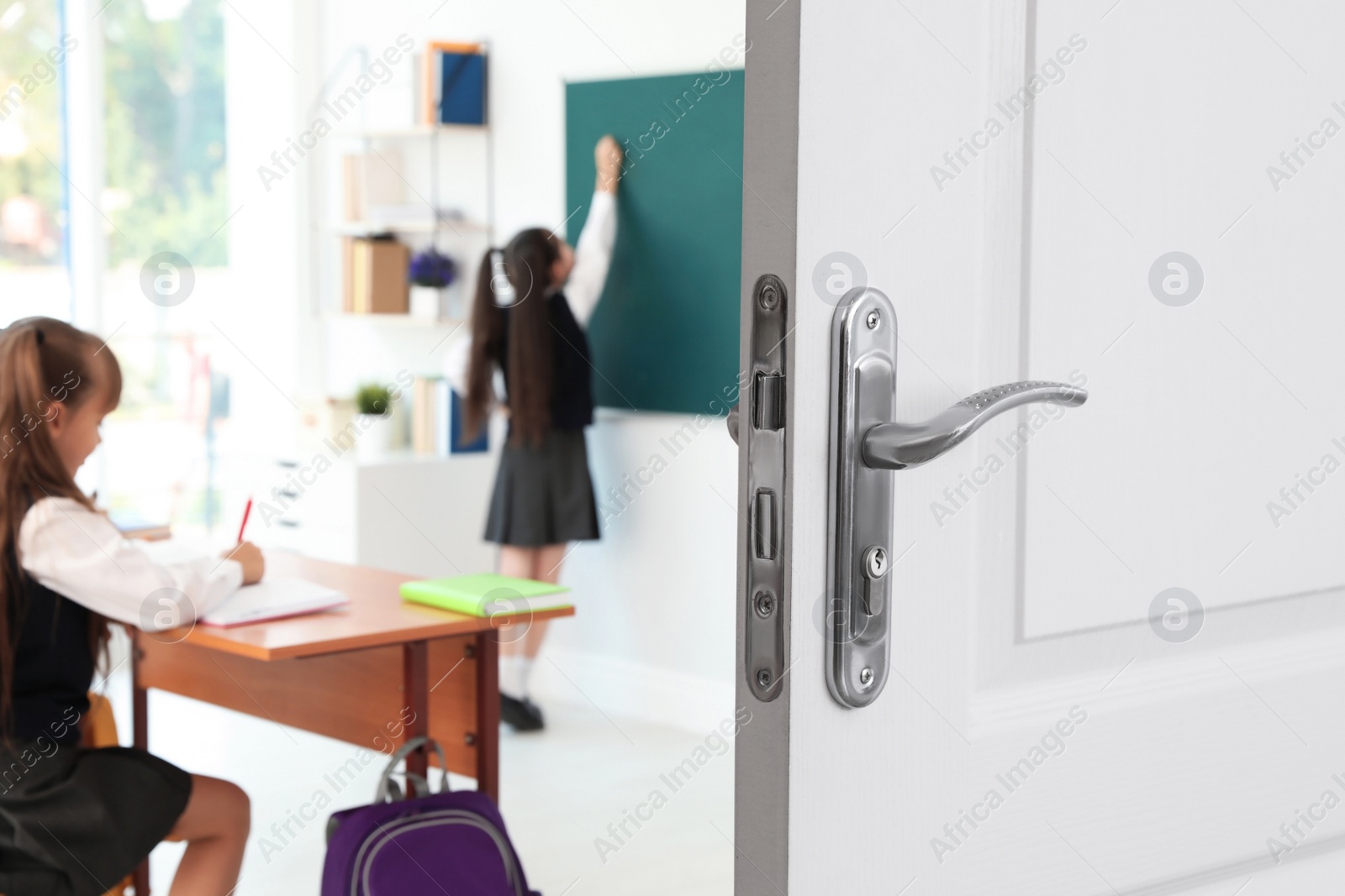 Image of Wooden door open into modern classroom with students