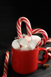 Photo of Cup of tasty cocoa with marshmallows and Christmas candy canes on black wooden table