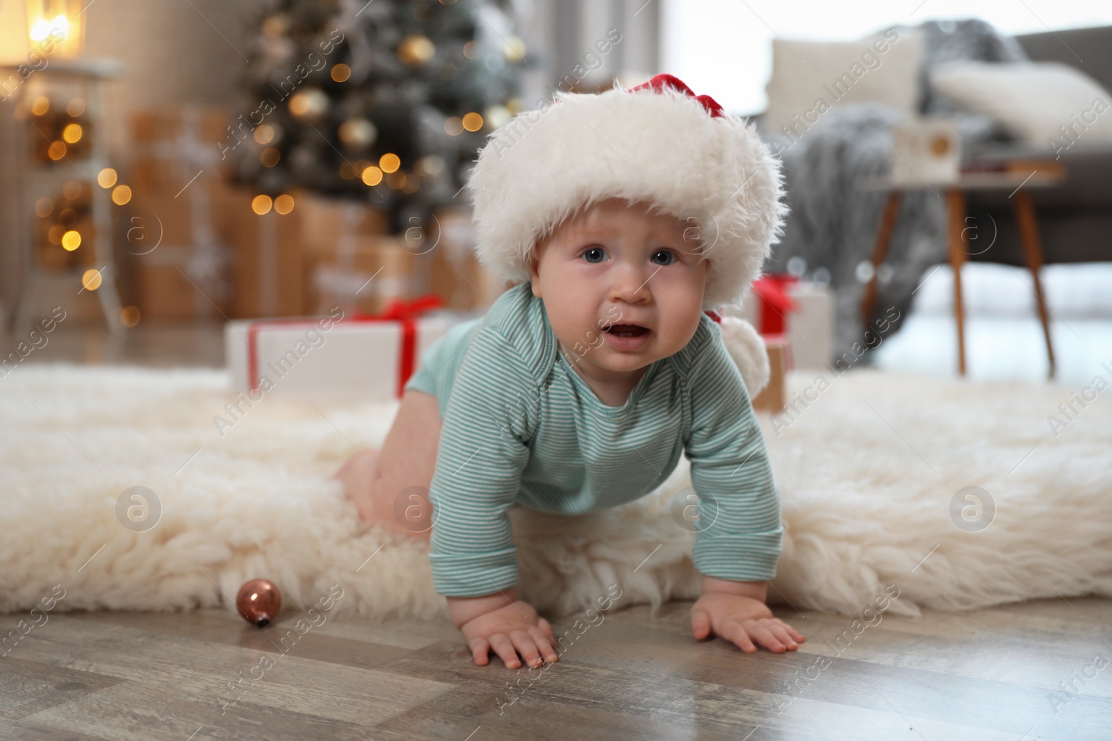 Image of Cute baby in Santa hat crawling on floor. First Christmas