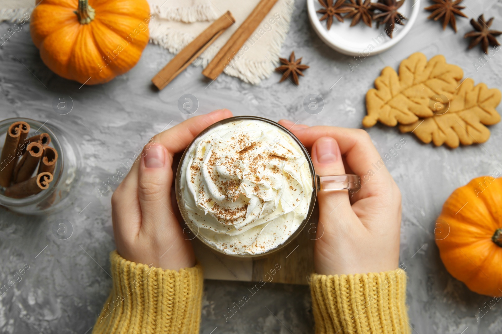 Photo of Woman holding cup of pumpkin spice latte with whipped cream at light grey table, top view