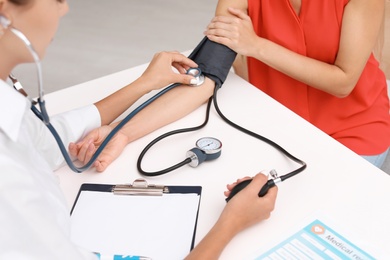 Photo of Doctor checking patient's blood pressure at table in office