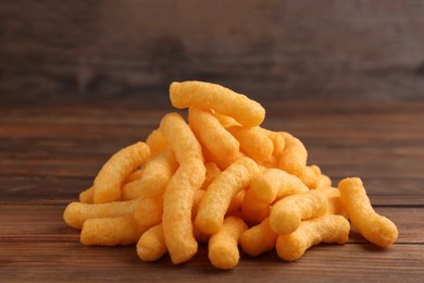 Photo of Heap of tasty cheesy corn puffs on wooden table