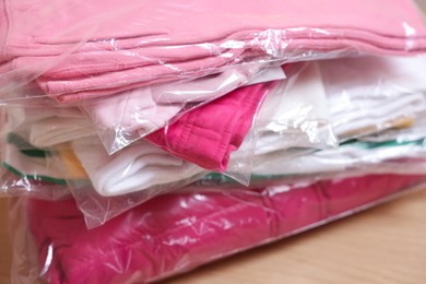 Photo of Stack of folded clothes in plastic bags on table, closeup