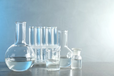 Laboratory glassware with liquid samples for analysis on grey table against toned blue background