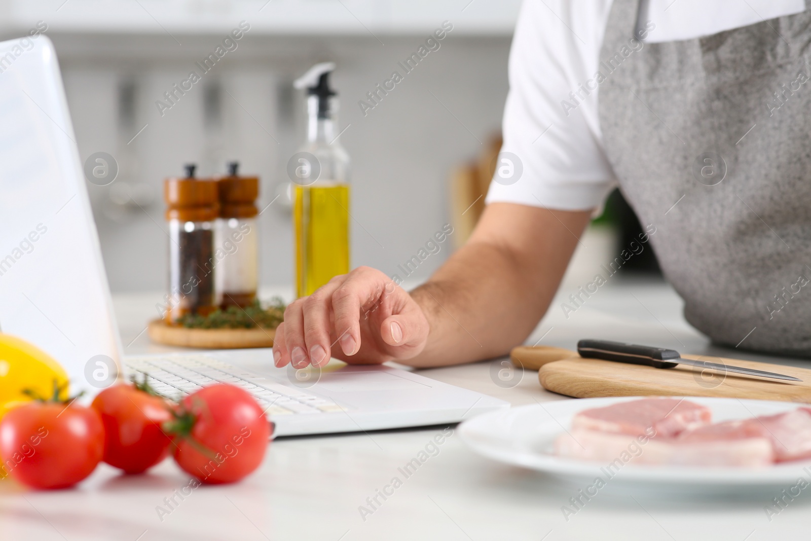 Photo of Man making dinner while watching online cooking course via laptop in kitchen, closeup