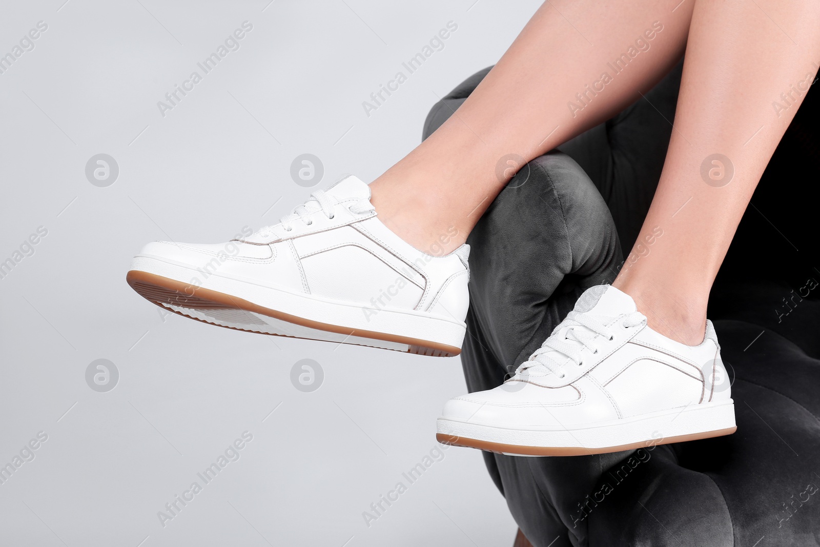 Photo of Woman with stylish sport shoes sitting in armchair on light background