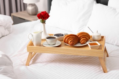 Photo of Wooden tray with tasty breakfast on bed at home
