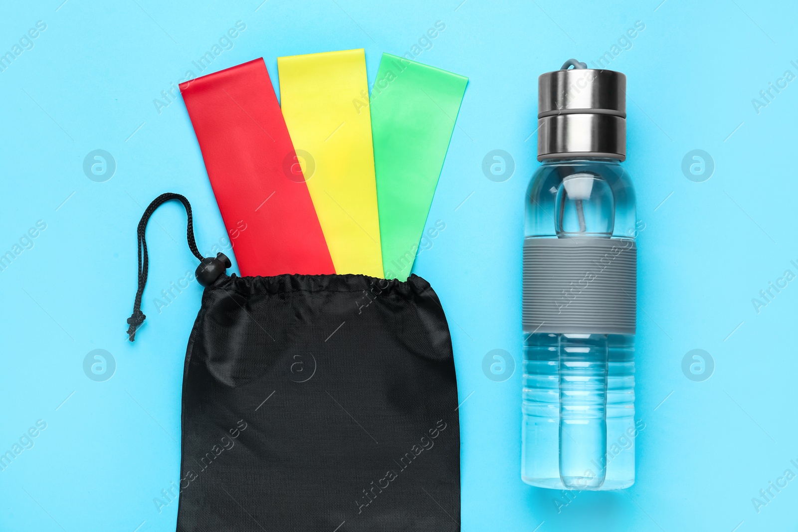 Photo of Set of fitness elastic bands and water bottle on light blue background, flat lay