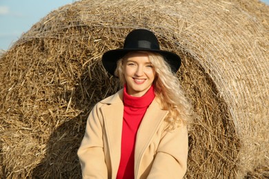 Beautiful woman sitting near hay bale outdoors. Autumn season