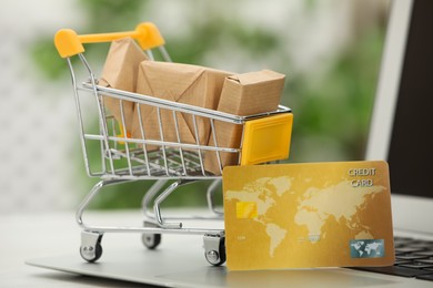 Photo of Online payment concept. Small shopping cart with bank card, boxes on laptop, closeup