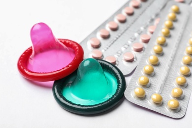 Photo of Condoms and birth control pills on white background, closeup. Safe sex concept