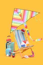 Photo of Deck chair, kite, suitcases and beach accessories against orange background. Summer vacation