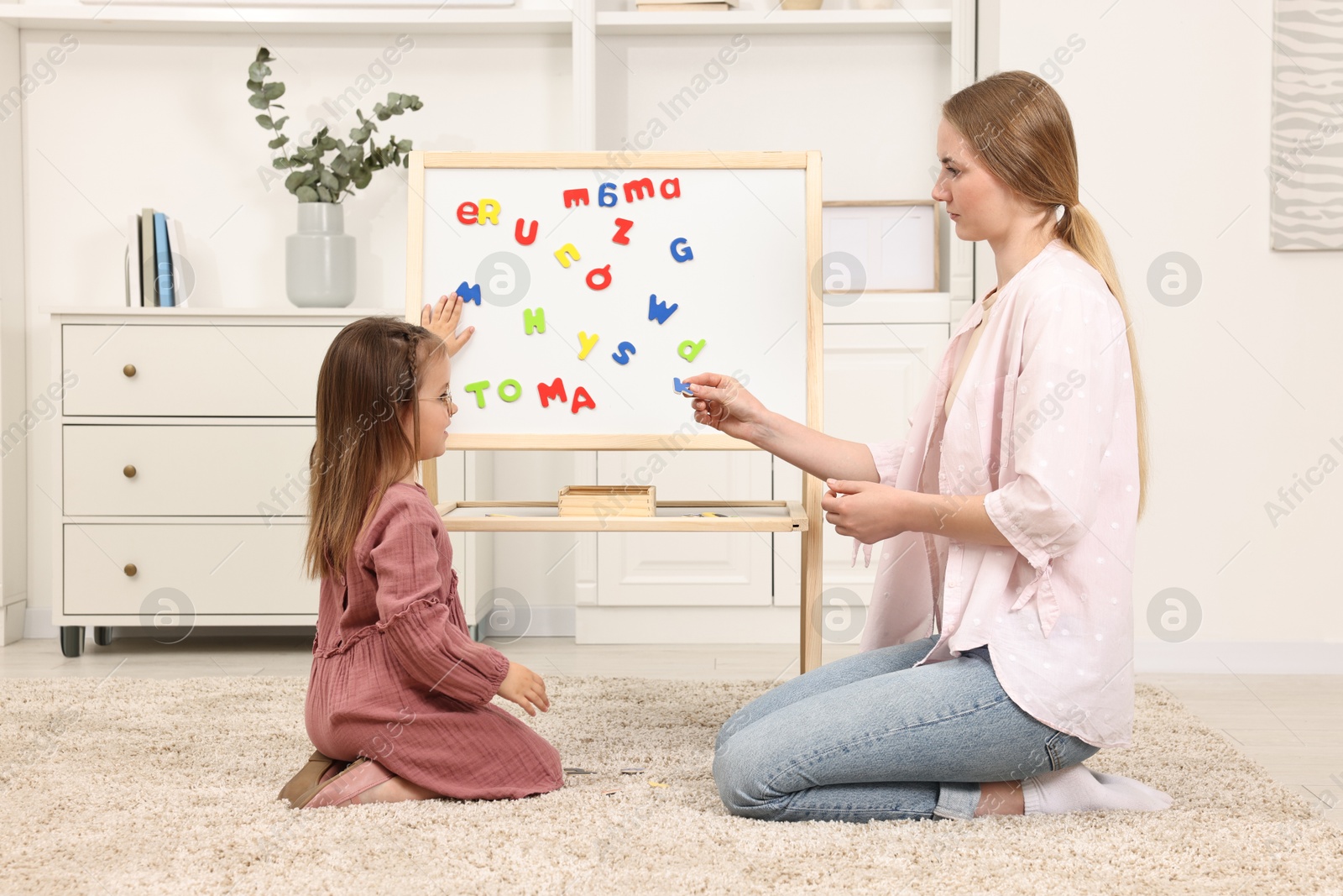 Photo of Mom teaching her daughter alphabet with magnetic letters at home