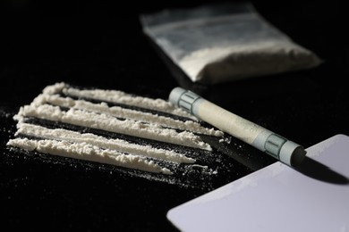 Photo of Drug addiction. Cocaine, rolled dollar banknote and blank card on black table, closeup