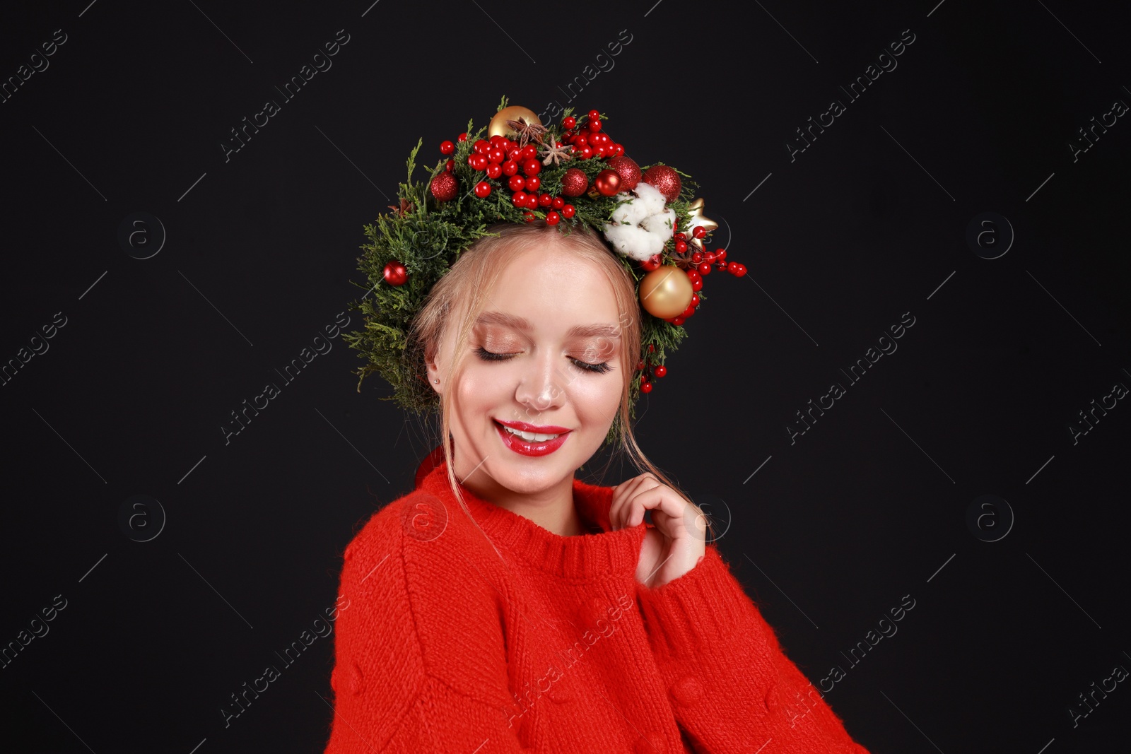 Photo of Beautiful young woman wearing Christmas wreath on black background