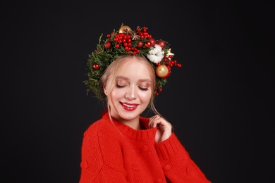 Photo of Beautiful young woman wearing Christmas wreath on black background