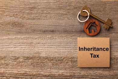 Photo of Inheritance Tax. Card and key with key chain in shape of house on wooden table, flat lay. Space for text