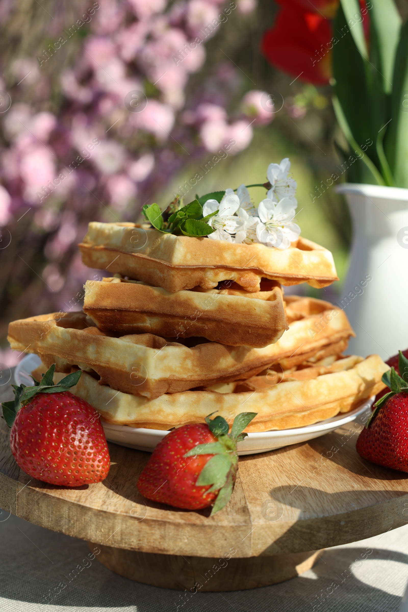 Photo of Freshly baked waffles and beautiful bouquet of tulips on table in garden, closeup