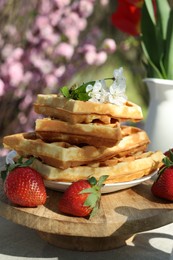 Freshly baked waffles and beautiful bouquet of tulips on table in garden, closeup
