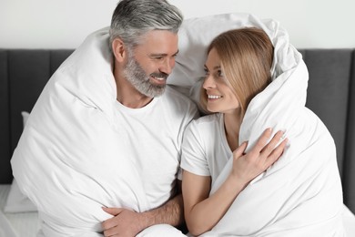 Lovely mature couple wrapped in blanket on bed at home