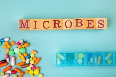 Word Microbes made with wooden cubes, many pills and box on light blue background, top view