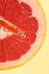 Photo of Dripping cosmetic serum from pipette onto grapefruit slice against yellow background, top view