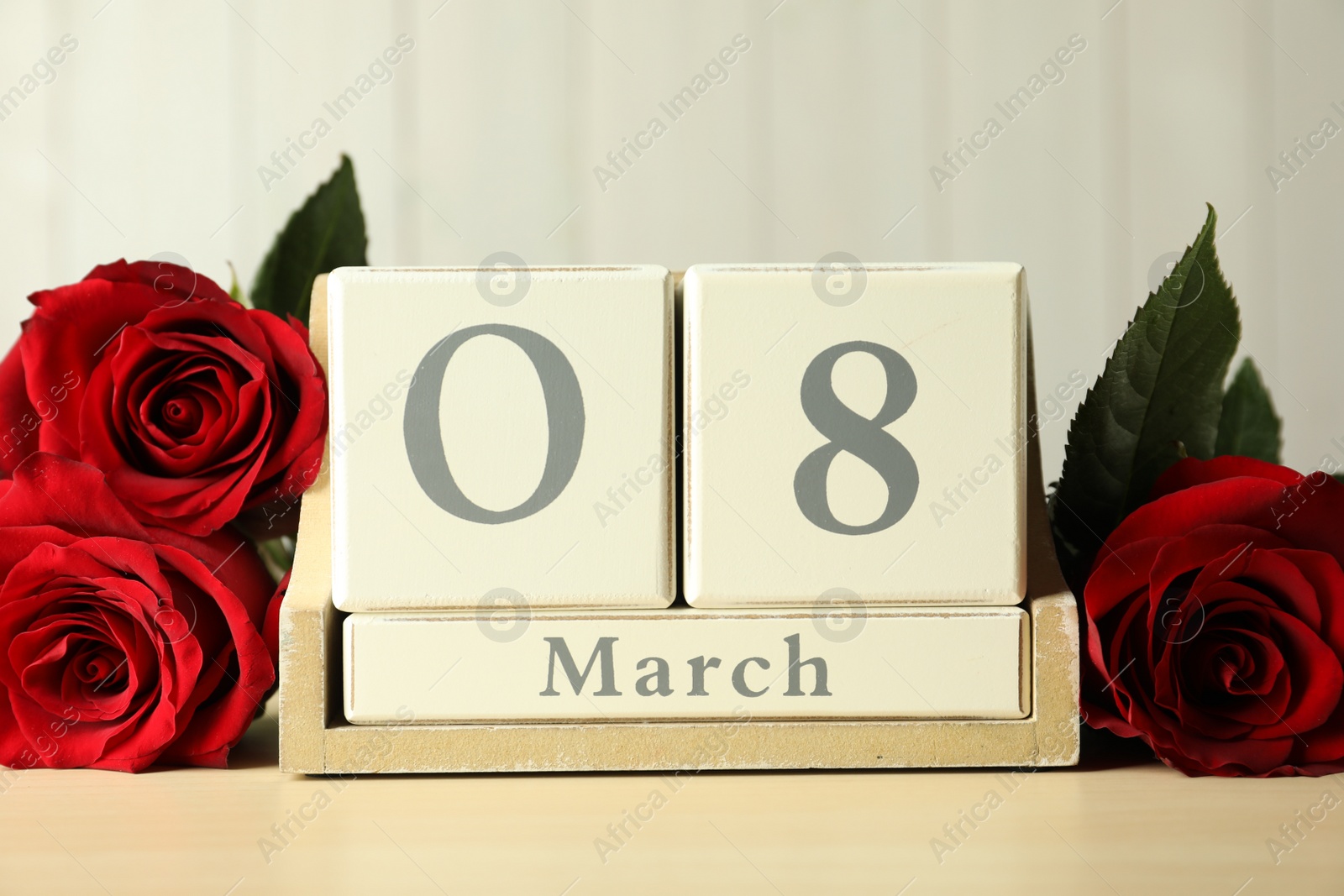 Photo of Wooden block calendar with date 8th of March and roses on table against light background. International Women's Day