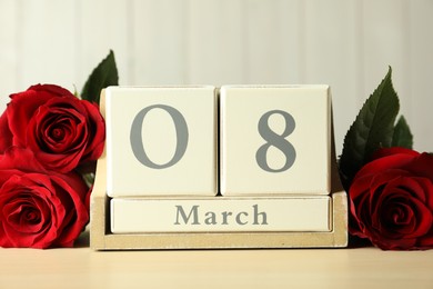 Photo of Wooden block calendar with date 8th of March and roses on table against light background. International Women's Day