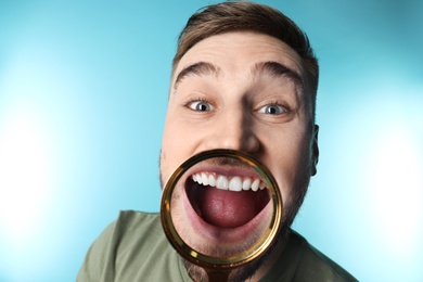 Photo of Young man with healthy teeth and magnifier on color background