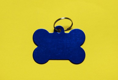 Photo of Blue metal pet tag in shape of bone with ring on yellow background, top view. Space for text